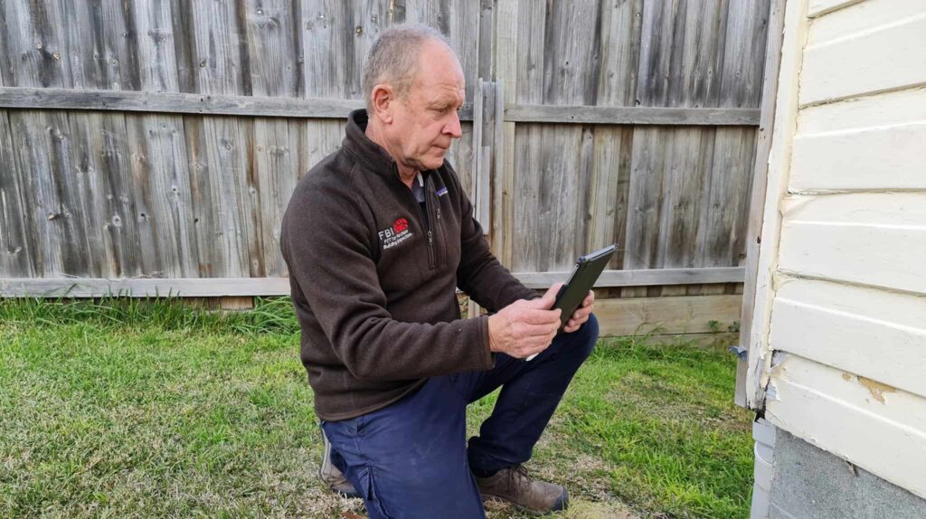 Peter Genders from fearless Building Inspections holding a tablet taking a photo of a damaged house